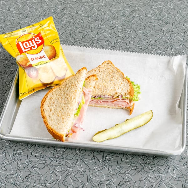 A ham sandwich with lettuce and red onion, a pickle spear, and Lay's chips on a tray.