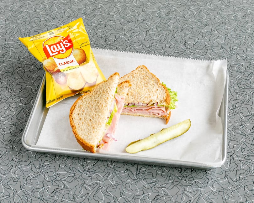 A ham sandwich with lettuce and red onion, a pickle spear, and Lay's chips on a tray.