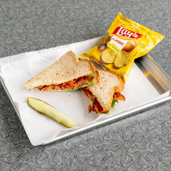 A bacon, lettuce, and tomato sandwich with a pickle spear and Lay's potato chips on a tray.
