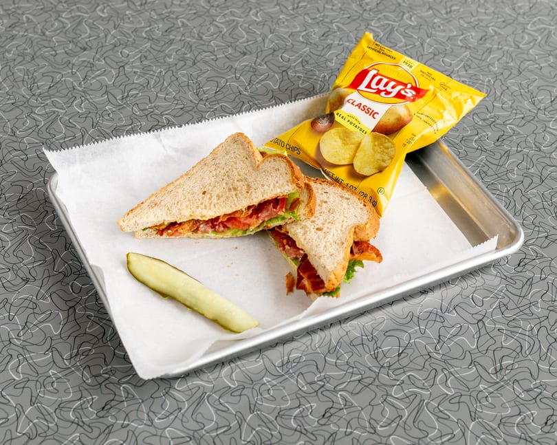 A bacon, lettuce, and tomato sandwich with a pickle spear and Lay's potato chips on a tray.