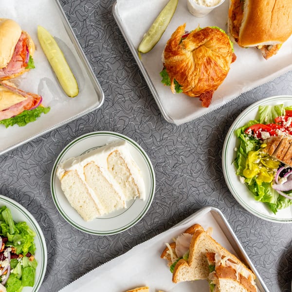 Overhead view of various sandwiches, salads, and a slice of cake on a patterned gray table.