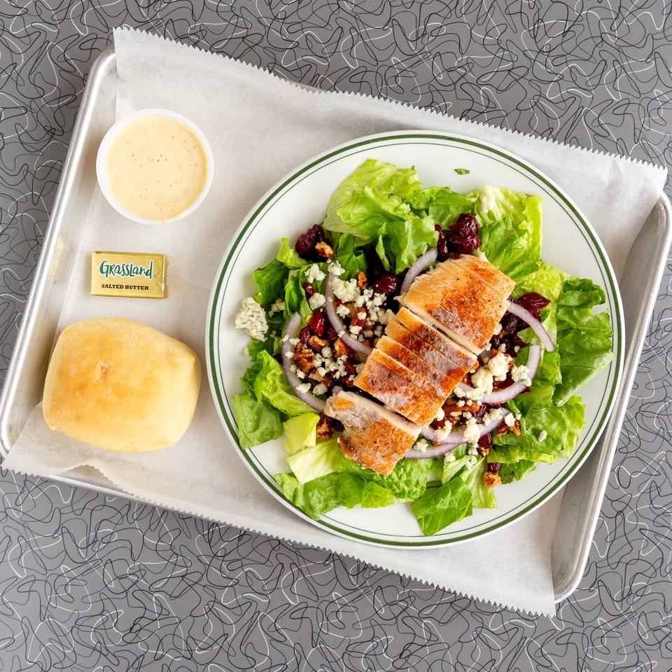 Overhead view of a grilled chicken salad with cranberries, blue cheese, and red onion.