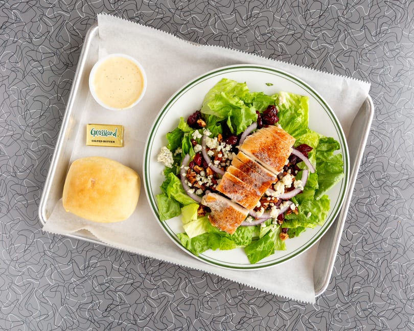 Overhead view of a grilled chicken salad with cranberries, blue cheese, and red onion.