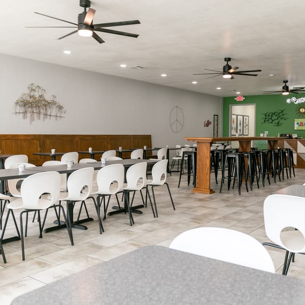 Spacious restaurant dining area with white chairs, dark tables, a green accent wall, and ceiling fans.