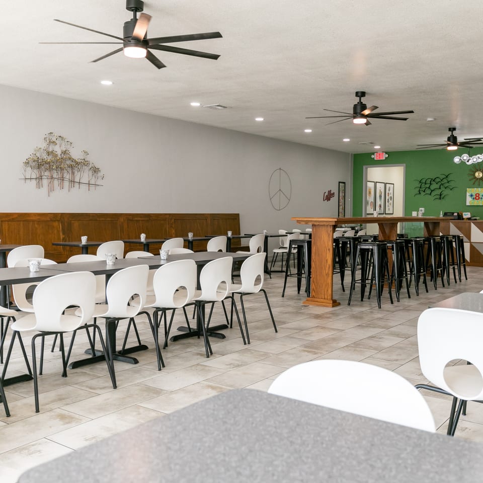 Spacious restaurant dining area with white chairs, dark tables, a green accent wall, and ceiling fans.
