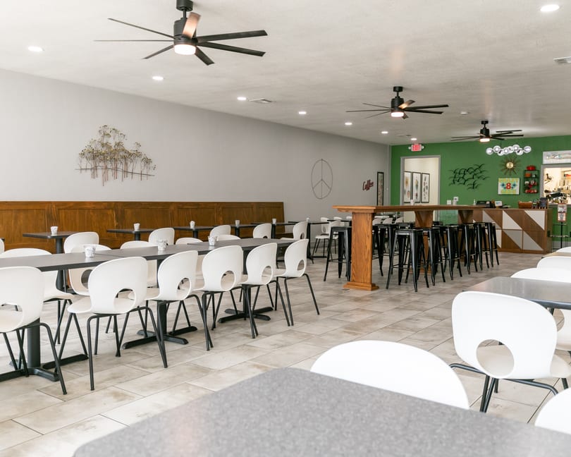 Spacious restaurant dining area with white chairs, dark tables, a green accent wall, and ceiling fans.