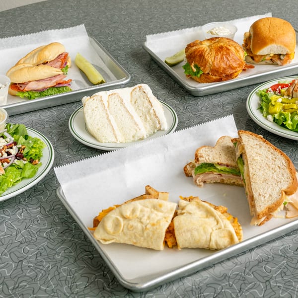 A full table of sandwiches, salads, and a slice of cake on a retro patterned table.