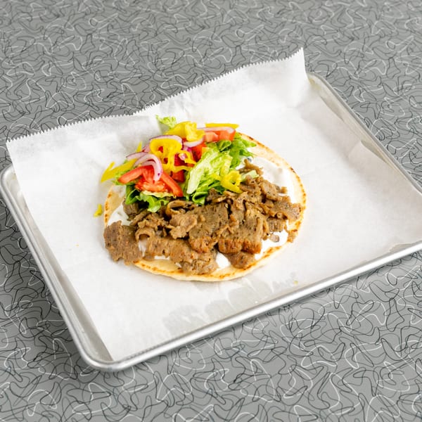Gyro on a metal tray with white paper, featuring meat, lettuce, tomatoes, onions, and yellow peppers.