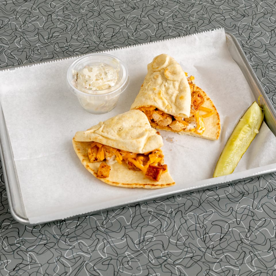 Two chicken and cheese pita wraps, a side of coleslaw, and a pickle spear on a tray.
