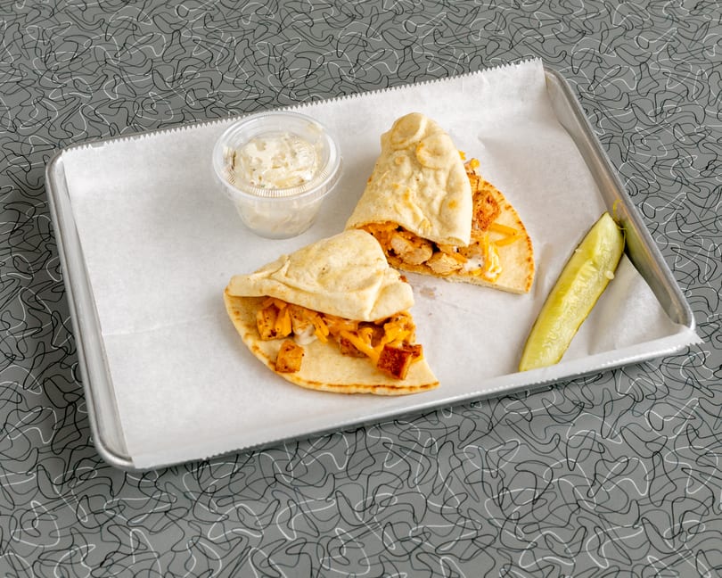 Two chicken and cheese pita wraps, a side of coleslaw, and a pickle spear on a tray.