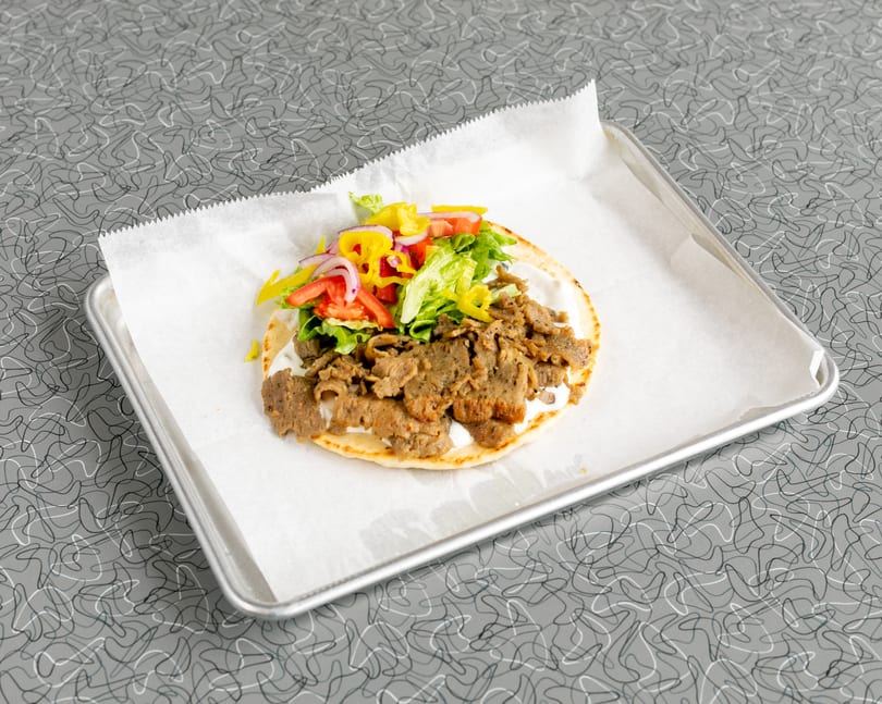 Gyro meat, lettuce, tomatoes, red onions, and yellow peppers on pita bread with white sauce.