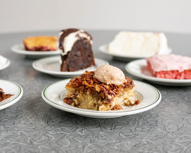 Various dessert slices, including pecan pie, chocolate cake, and strawberry cake, on white plates.