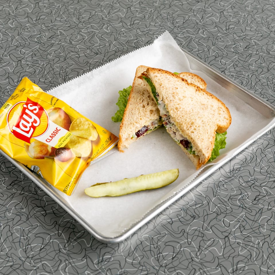 A chicken salad sandwich, Lay's potato chips, and a pickle spear on a metal tray.