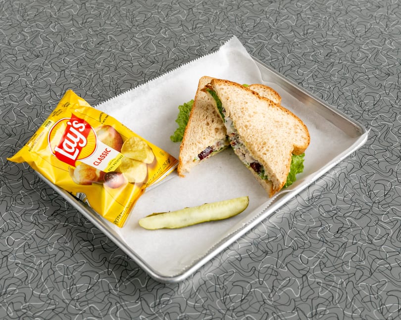 A chicken salad sandwich, Lay's potato chips, and a pickle spear on a metal tray.
