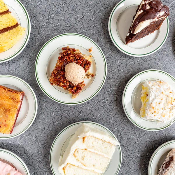 Assortment of dessert slices, including cakes, pies, and brownies, on a diner-style tabletop.