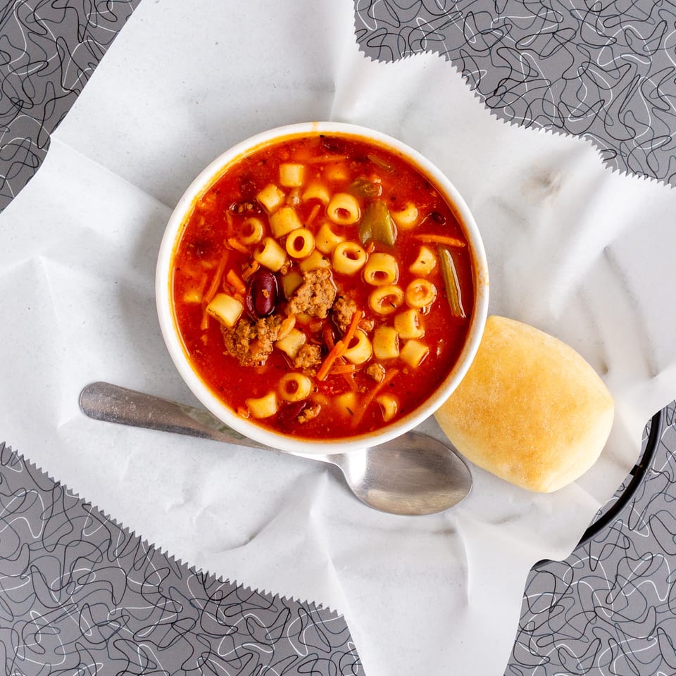 Hearty minestrone soup with pasta, beans, and vegetables, served with a bread roll.