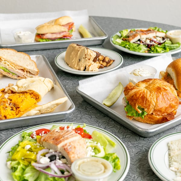 A table filled with various sandwiches, salads, and a dessert on plates and metal trays.