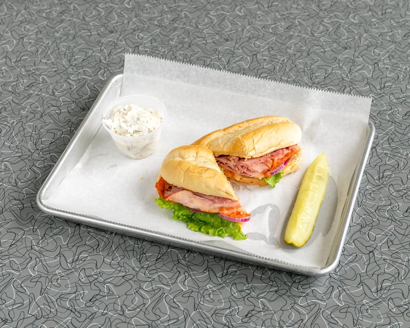 Ham and salami sub sandwich with lettuce, red onion, a pickle spear, and coleslaw.