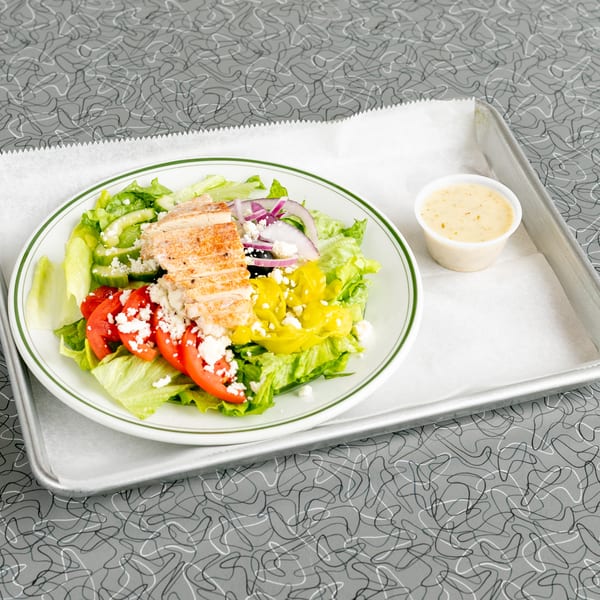 Grilled chicken salad with lettuce, tomatoes, cucumbers, red onion, feta, and dressing on a tray.
