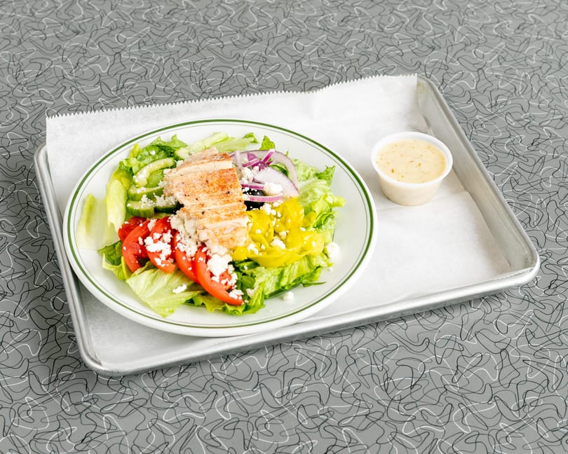 Grilled chicken salad with lettuce, tomatoes, cucumbers, red onion, feta, and dressing on a tray.