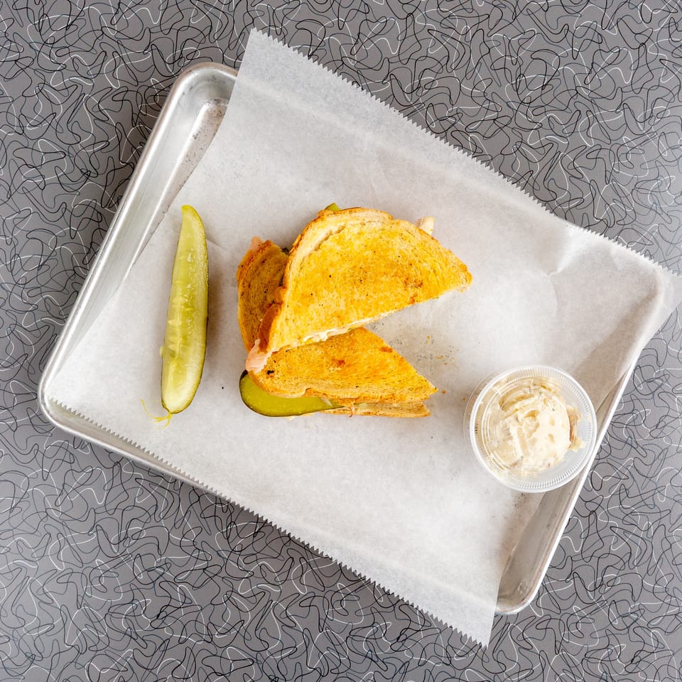 Grilled sandwich halves, a pickle spear, and a side of potato salad on a metal tray.